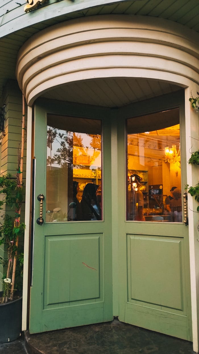 Services Inviting green doors open to a cozy cafe with warm lighting, creating an urban charm.